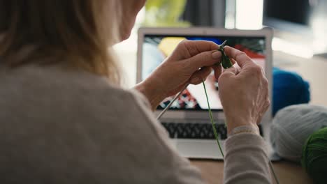 close up of caucasian senior woman at home learning how to knit from video tutorial.