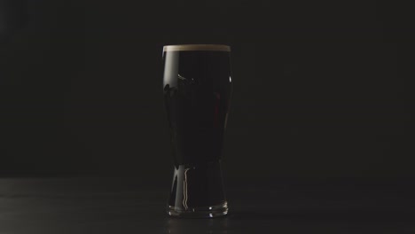 pint of irish stout in glass against black studio background to celebrate st patricks day