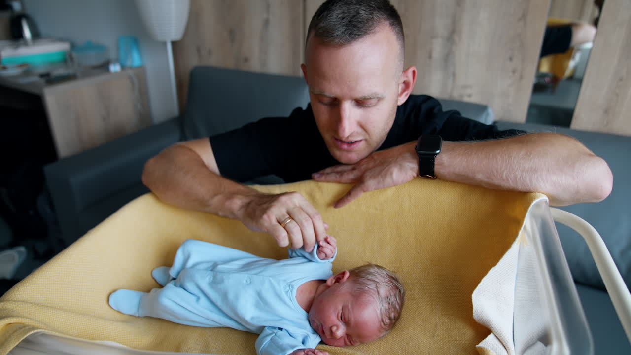 Caucasian dad sitting over the crib with his newborn. Father is talking to his son and touching him with tenderly.