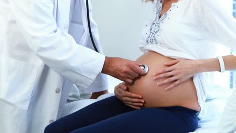 médico examinando el vientre de una mujer embarazada con un estetoscopio en la sala