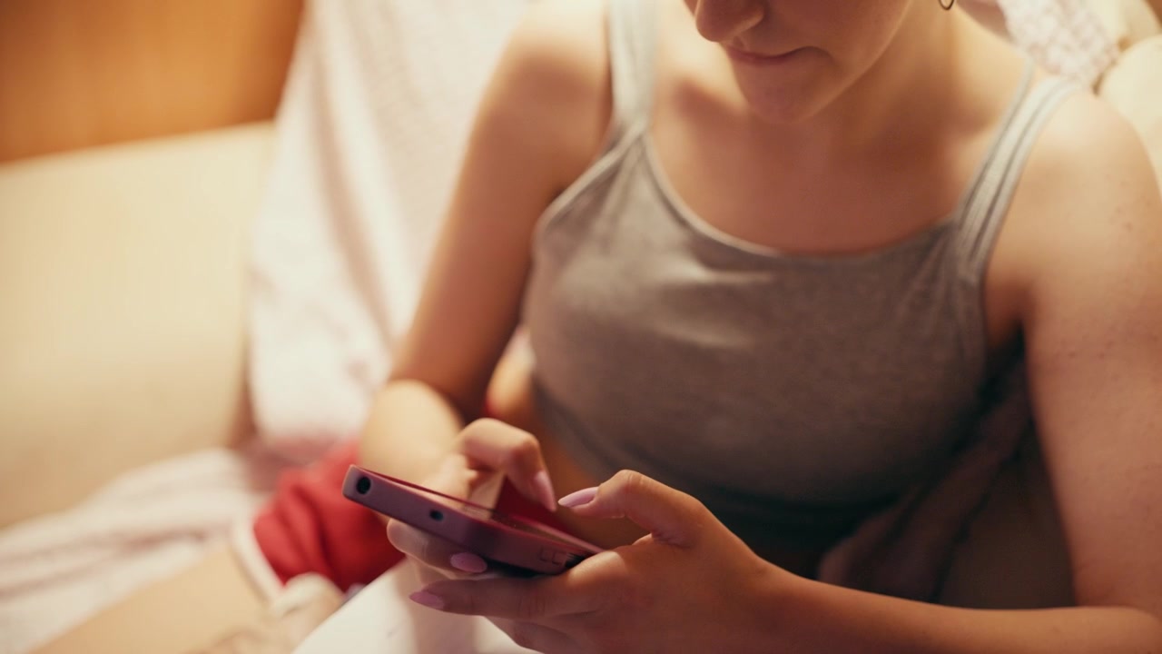 Ragazza delle scuole superiori concentrata, seduta su un divano, digita sul suo telefono cellulare, usando uno smartphone per copiare appunti, cercare risposte d'esame o barare a un test futuro mentre studia a casa.