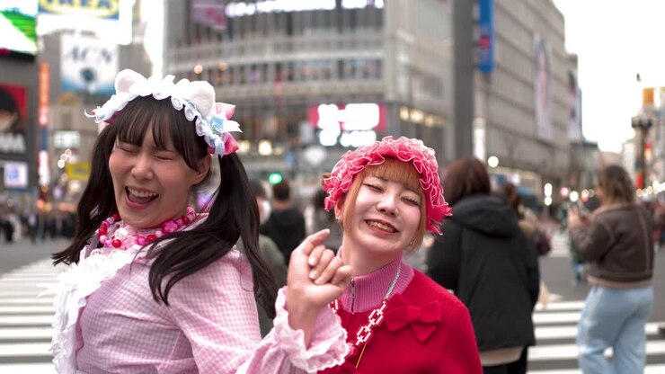 Due donne che indossano colorati abiti in stile decora ridono e ballano all'affollato incrocio di Shibuya.