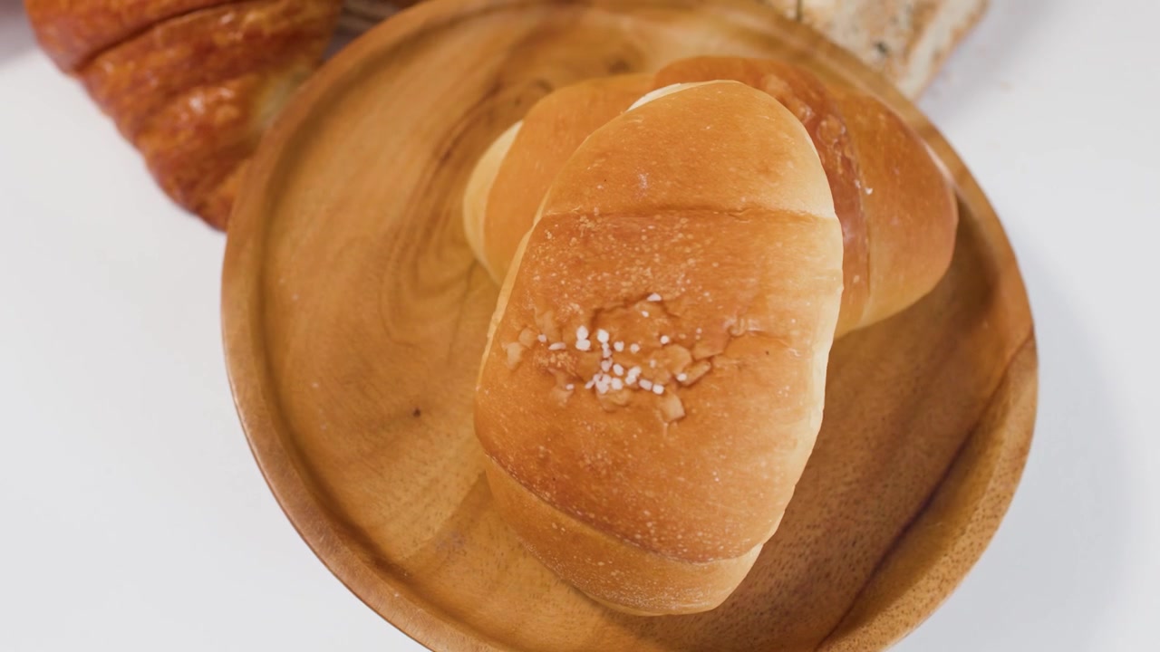 Hand Placing Fresh Salt Bread Roll on Wooden Plate