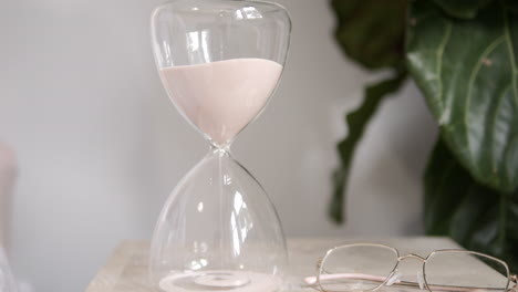 Hourglass-Sands-Fall-On-Bedside-Table-In-Sunlit-Room,-SLOW-MOTION