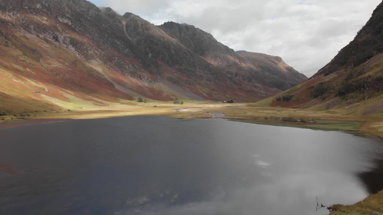 주변 계곡과 산을 드러내는 스코틀랜드 글렌코에 있는 고원 호수 위로 뒤로 날아갑니다.