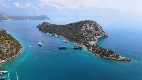 Beim-Flug-Der-Drohne-über-Der-Bucht-Im-Mittelmeer,-In-Der-Sich-Die-Insel-Befindet,-Schweben-Yachten-Vor-Der-Kulisse-Von-Berglandschaften-Und-Blauem-Himmel