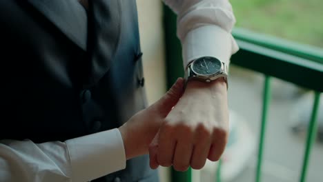close up of groom adjusting a silver wristwatch over white shirt and dark vest