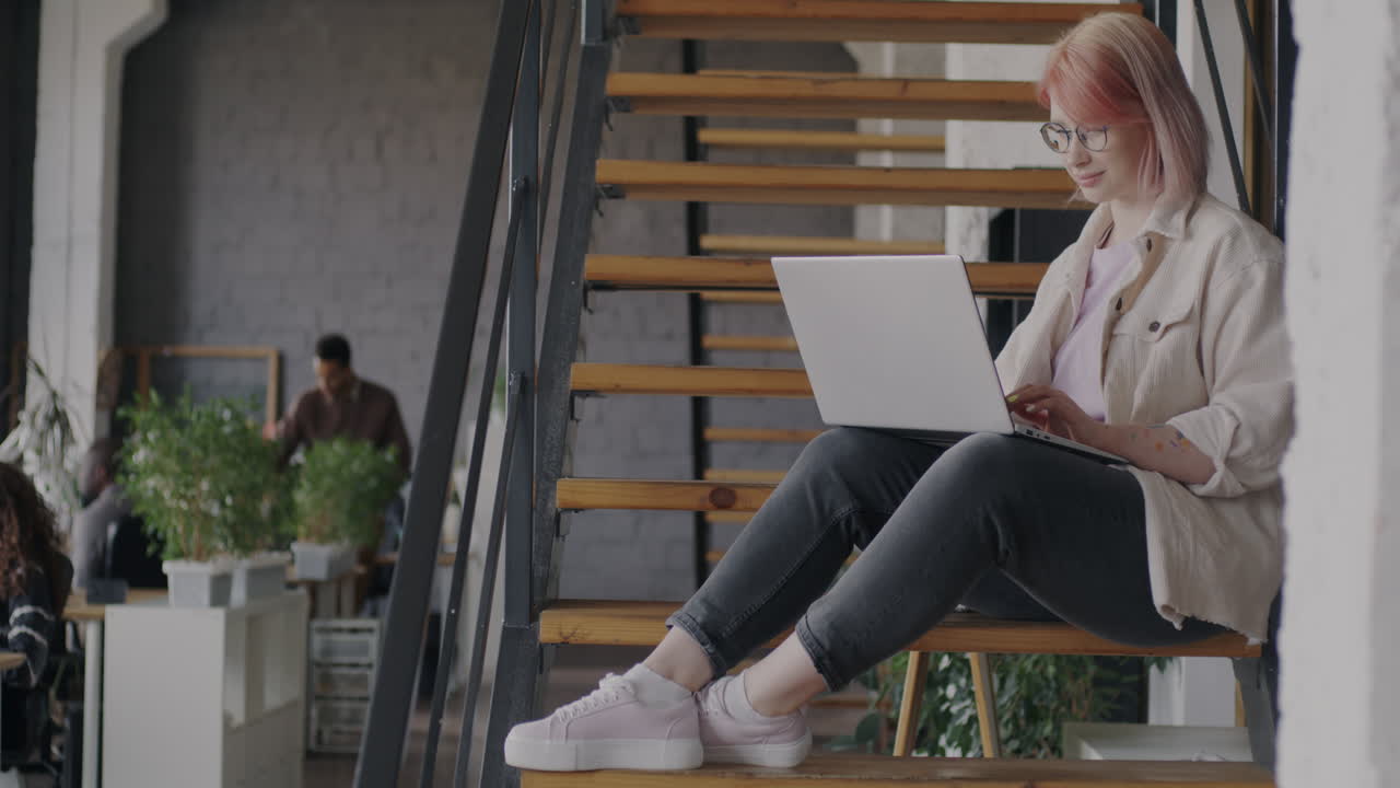 Woman Working on Laptop on Stairs in Modern Office