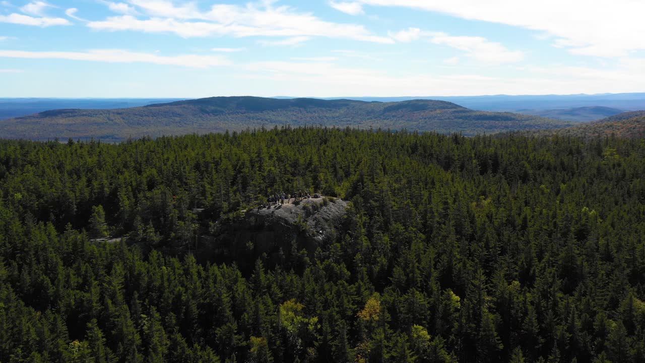 toma aérea de un dron que se aleja de un grupo de personas que caminan y se paran juntas admirando la vista desde un afloramiento rocoso en el desierto de maine