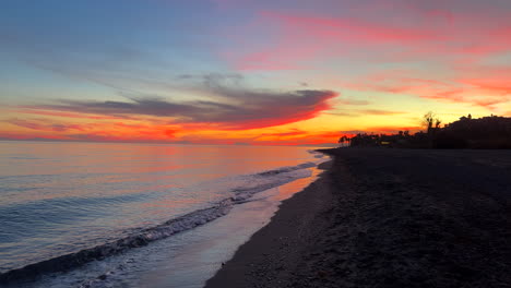 Pintoresca-Puesta-De-Sol-Especial-Rosa-Naranja-Púrpura-Junto-A-La-Playa-Con-Palmeras,-Vista-Al-Mar-Y-El-Peñón-De-Gibraltar-En-Marbella-España,-Olas-De-Agua,-Cielo-Mágico,-Toma-De-4k