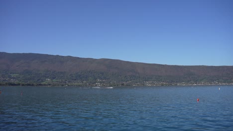 Water-skier-being-pulled-by-motorboat-on-Lake-Annecy-in-the-French-Alps,-Pan-right-follow-shot