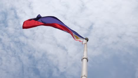 philippine national flag flying towards the the left captured from below and the sky is blue with fluffy cotton-like clouds