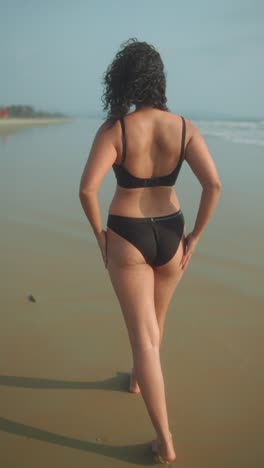 walking on the beach in a bikini, the woman enjoys the sun and the ocean breeze