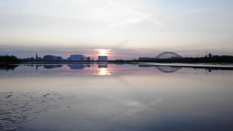 Sonnenaufgang-Hinter-Gebäuden,-Die-Sich-Wie-Ein-Spiegel-Auf-Dem-See-Spiegeln