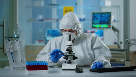 Scientist-in-ppe-suit-making-adjustments-and-looking-through-laboratory-microscope