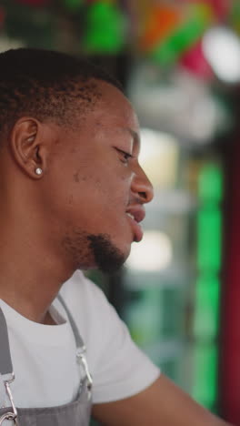 el camarero trabaja en el mostrador en un bar de primer plano. un joven afroamericano sirve bebidas a los huéspedes en una cafetería. un camarero negro con barba está en el mostradores