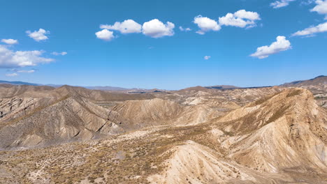 panoramic aerial rises above the eroded hills of tabernas desert and curves across the distinctive film industry landscapes crossing dry creek beds, craggy hills, and dust blown valleys