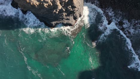 Toma-Aérea-Volando-Sobre-Olas-Turquesas-Que-Se-Estrellan-Contra-Acantilados-Escarpados-En-Un-Día-Soleado