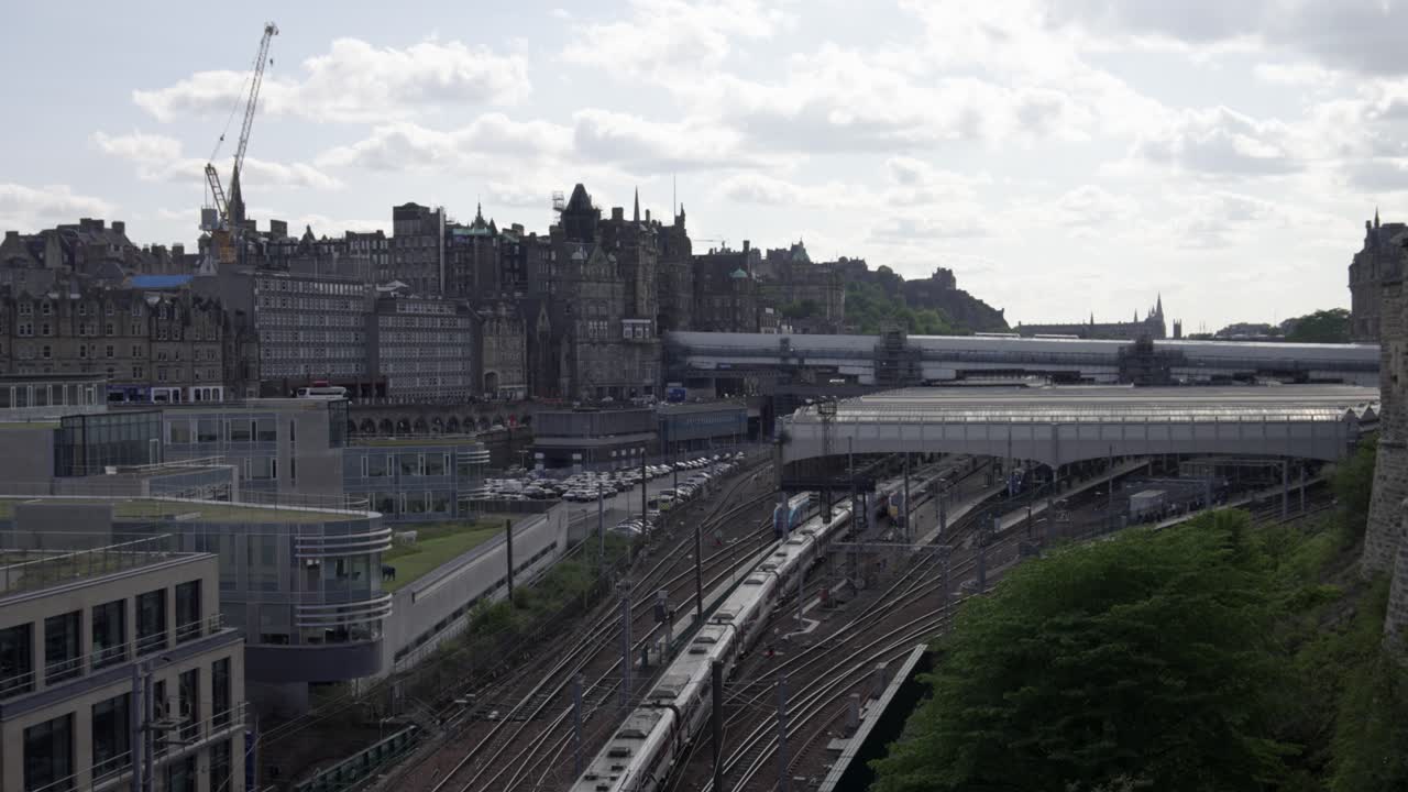 Aerial static of train arriving at Edinburgh Waverley Train Station with Edinburgh city centre in background, Scotland, UK