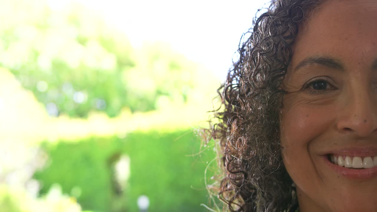 Una donna afroamericana apre gli occhi alla luce del sole, sorridendo verso la porta con un giardino in controluce, un orecchino a perno e spazio per il testo.