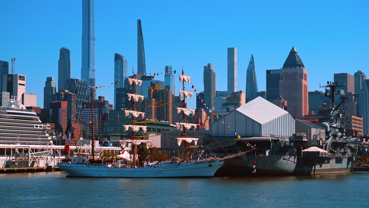 New York, USA, 2 ottobre 2025: Bellissima nave con le vele spiegate e bandiere colorate alla banchina. Grattacieli futuristici contro un cielo blu chiaro sullo sfondo.