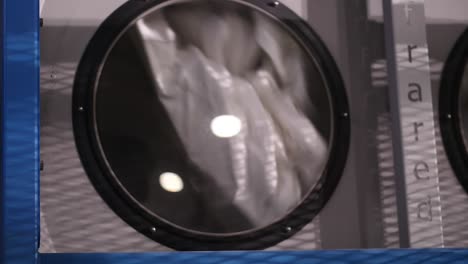 close up view looking through window of large industrial tumble dryer with white sheets inside