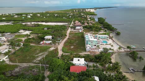 Drone-view-in-Belize-flying-over-caribbean-sea,-a-caye-covered-with-palm-trees-and-restaurants-on-a-cloudy-day