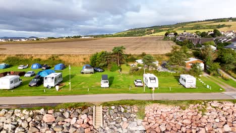 drone footage pans across a coastal caravan and camping site with motorhomes, tents, and cars under partly cloudy daylight in rosemarkie, scotland