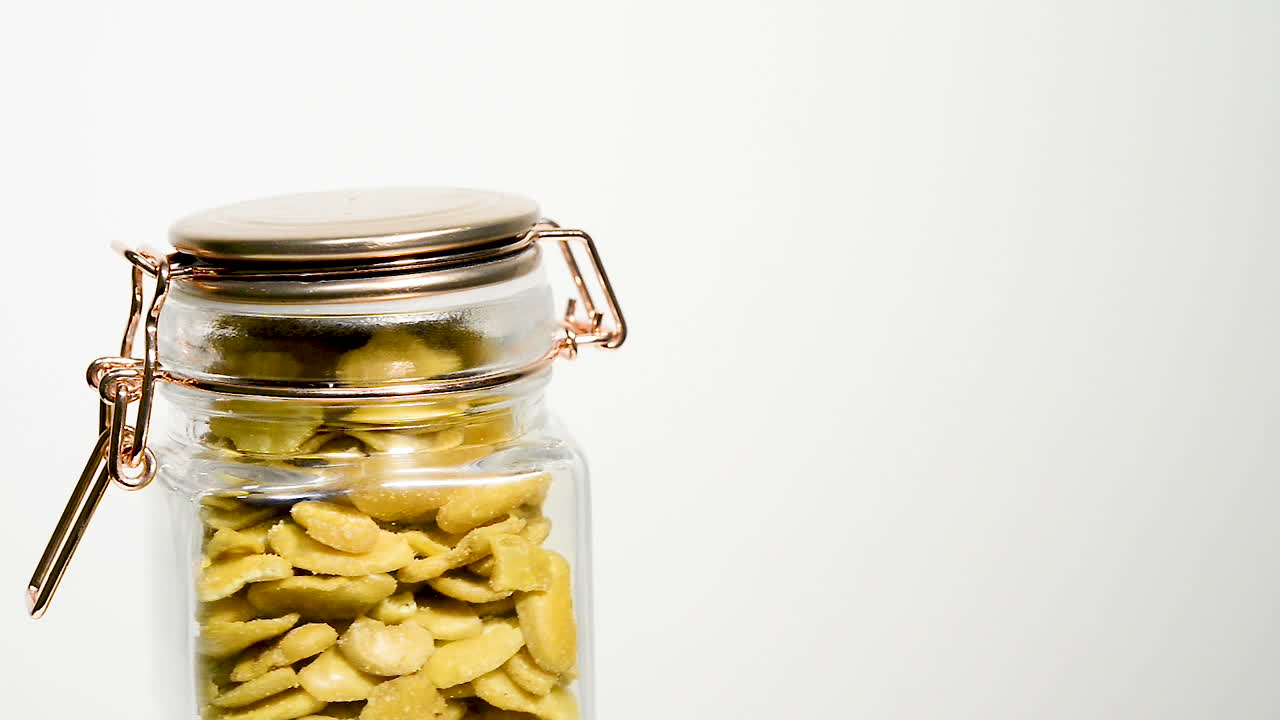 평범한 흰색 배경에 회전하는 구운 파바 콩으로 가득 찬 유리병