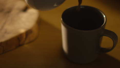 close up of steaming hot chocolate drink being poured into cup on table