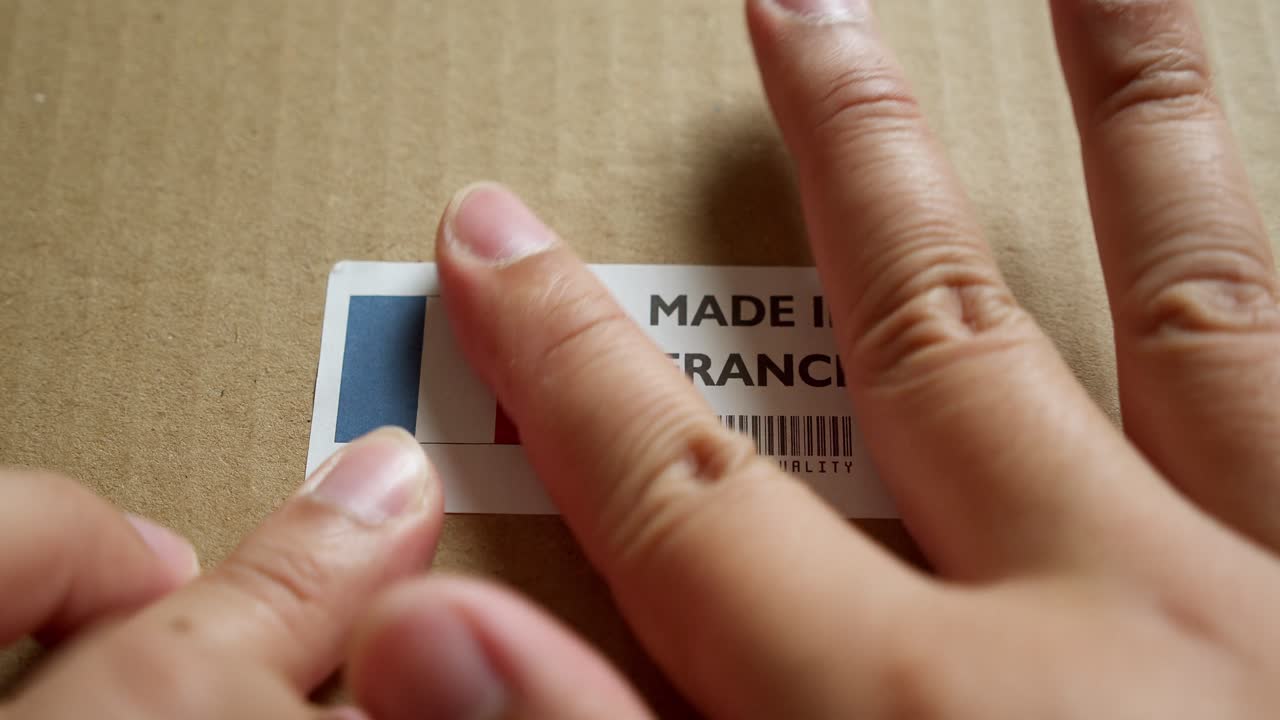 Hands applying MADE IN FRANCE flag label on a shipping box with product premium quality barcode