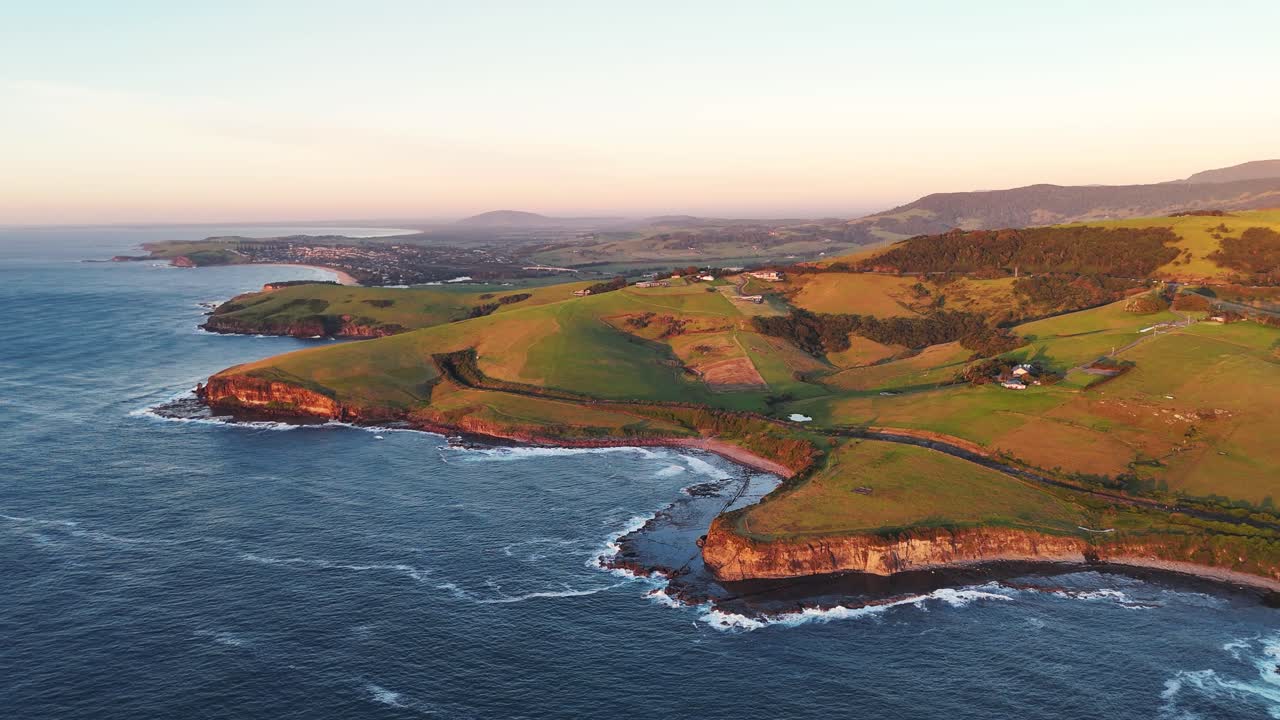 Cliffside waves crashing against rocks in Kiama, drone orbit at golden hour daylight