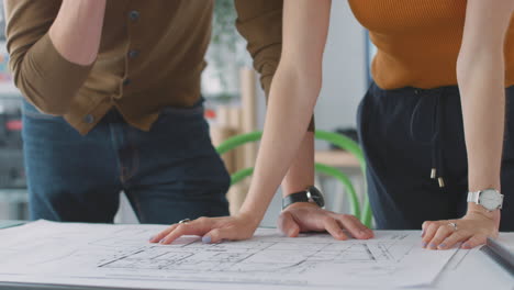 close up of male and female architects in office standing at desk and working on plans