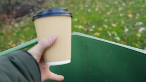 Woman's-hand-throwing-away-empty-paper-coffee-cup-in-recycling-bin