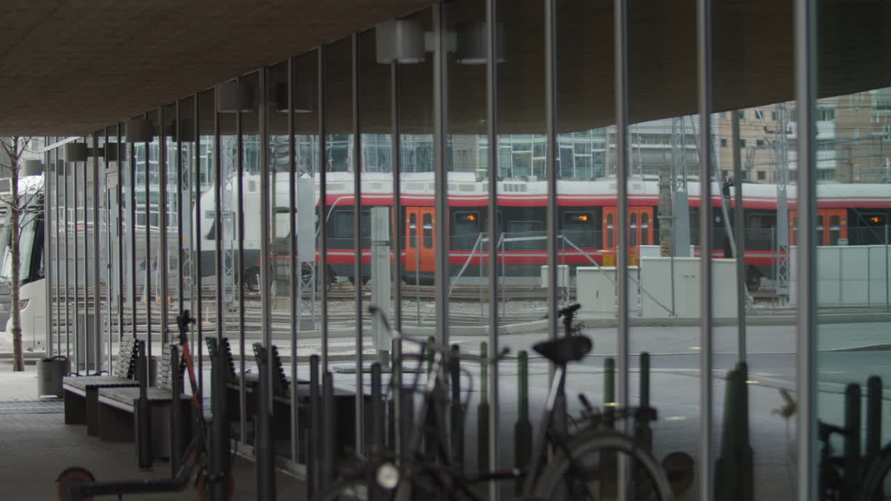 Slow motion medium wide 4K shot with parallax motion of window reflection of train leaving central commerce train station with bikes parked in foreground, in Barcode quarter of Bjørvika, Oslo Norway