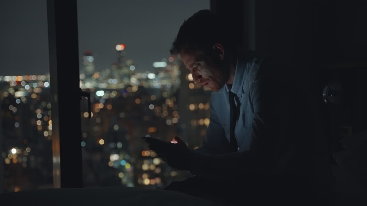 Man using phone in hotel room at night overlooking city