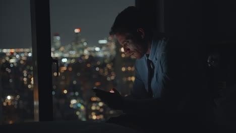 man using phone in hotel room at night overlooking city