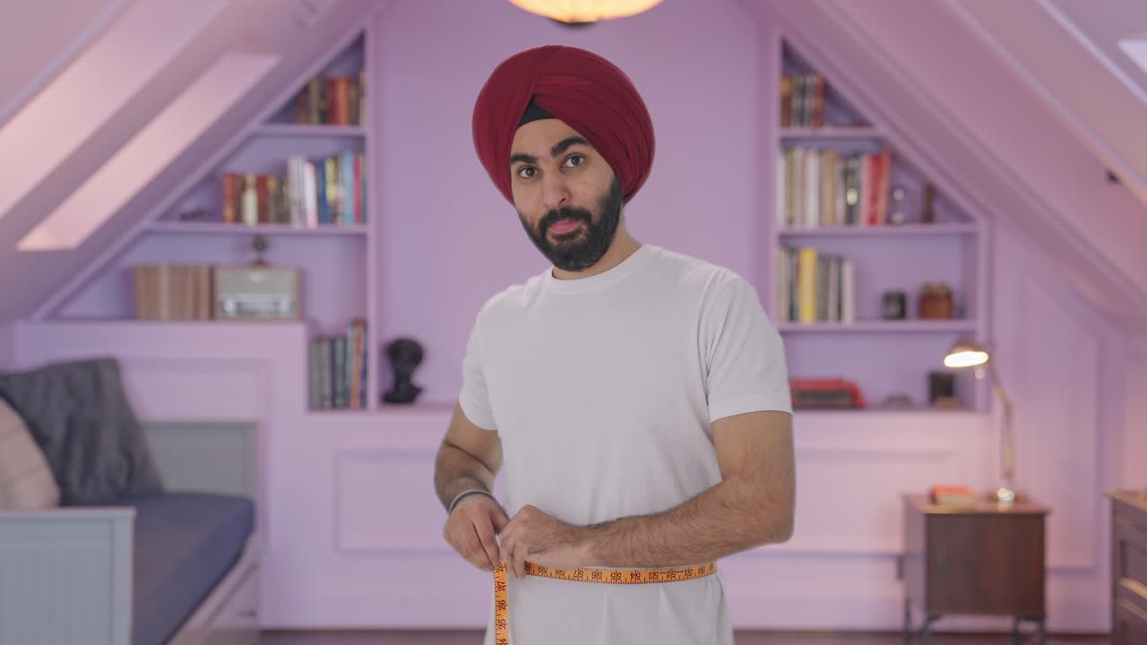 Uomo indiano Sikh felice che misura il girovita usando un metro a nastro