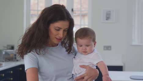 Close-Up-Of-Mother-With-Baby-Son-Working-From-Home-On-Laptop-In-Kitchen