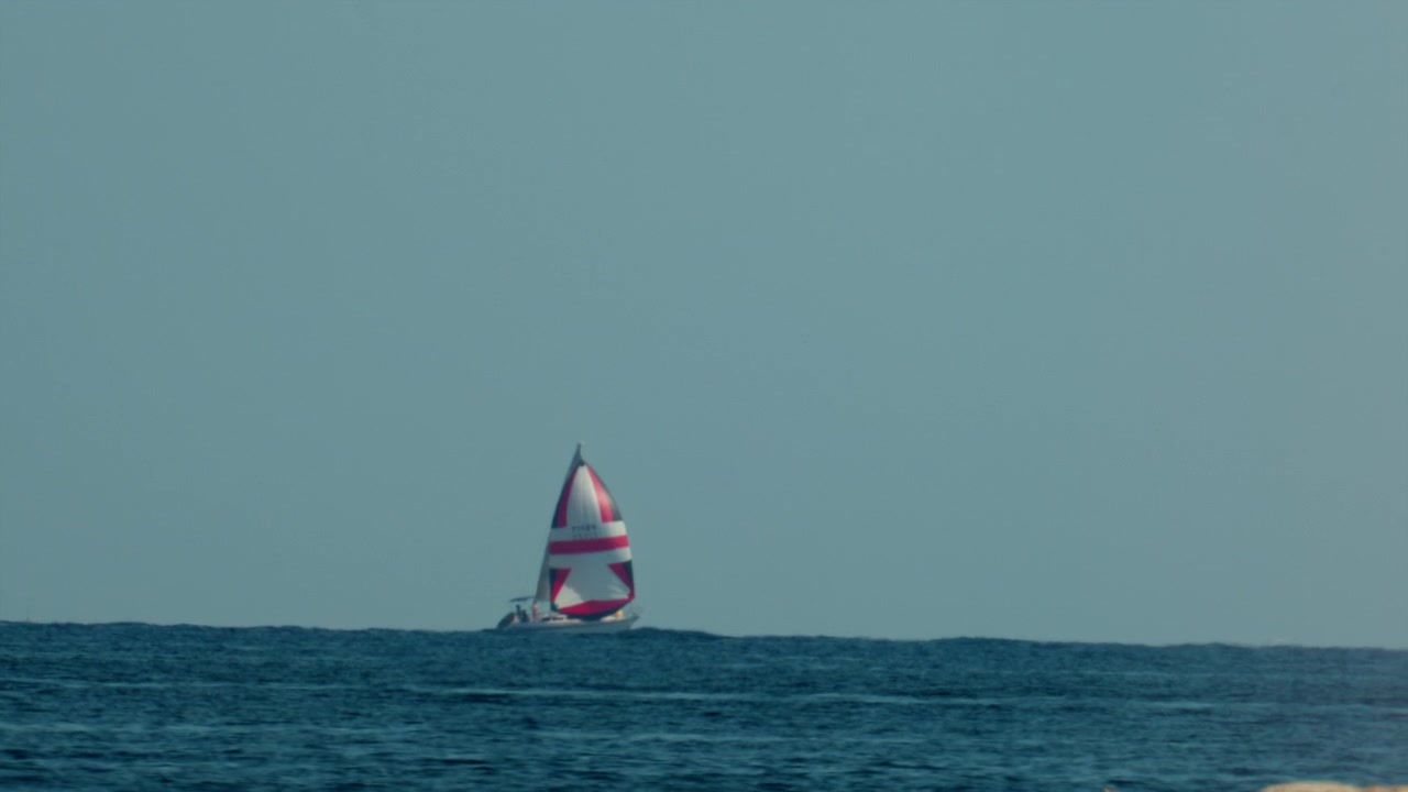 Sejlbåd med karakteristisk rød og hvid stjernesejl sejler på roligt blåt hav, illustrerer frihed, eventyr og sommerferie, Antibes, Frankrig