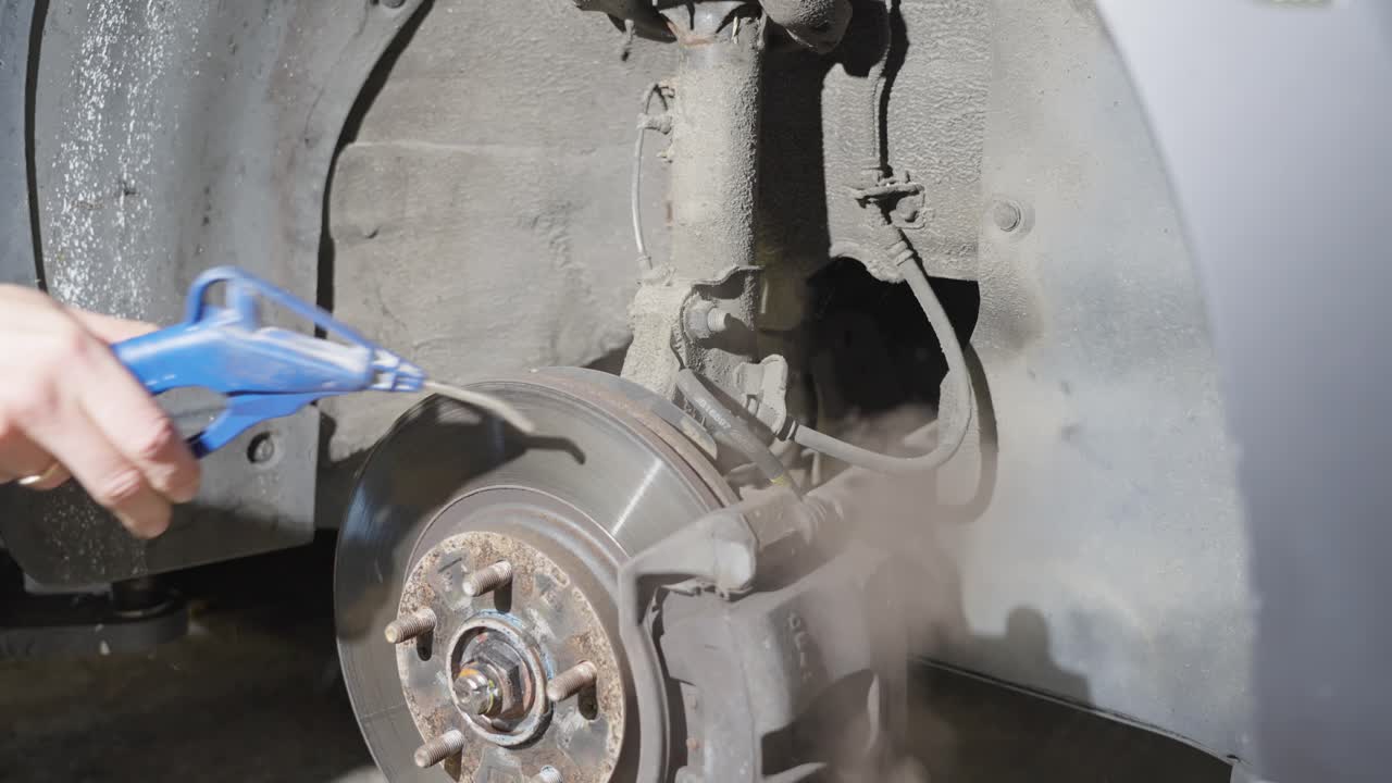 Man blows dirt off strut, area around rear wheel of car with air compressor and air gun, close up