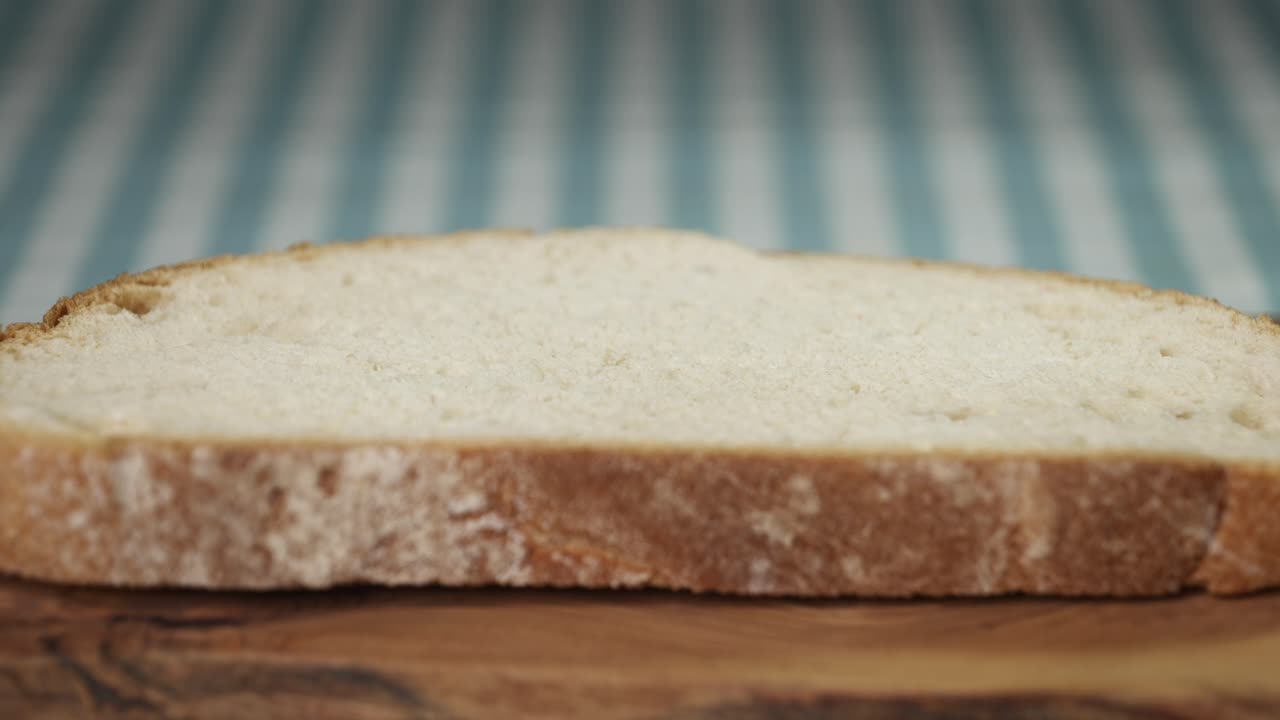 Close-up of a steady stream of extra virgin olive oil dripping onto a slice of artisan bread on a wooden board