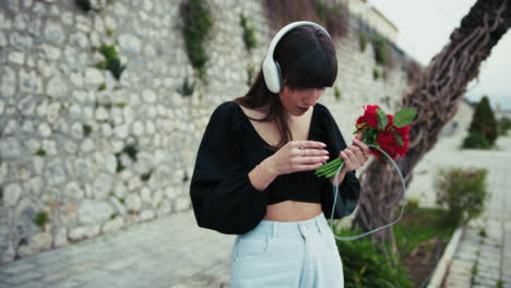 woman holding red flowers and listening to music outdoor in a little town