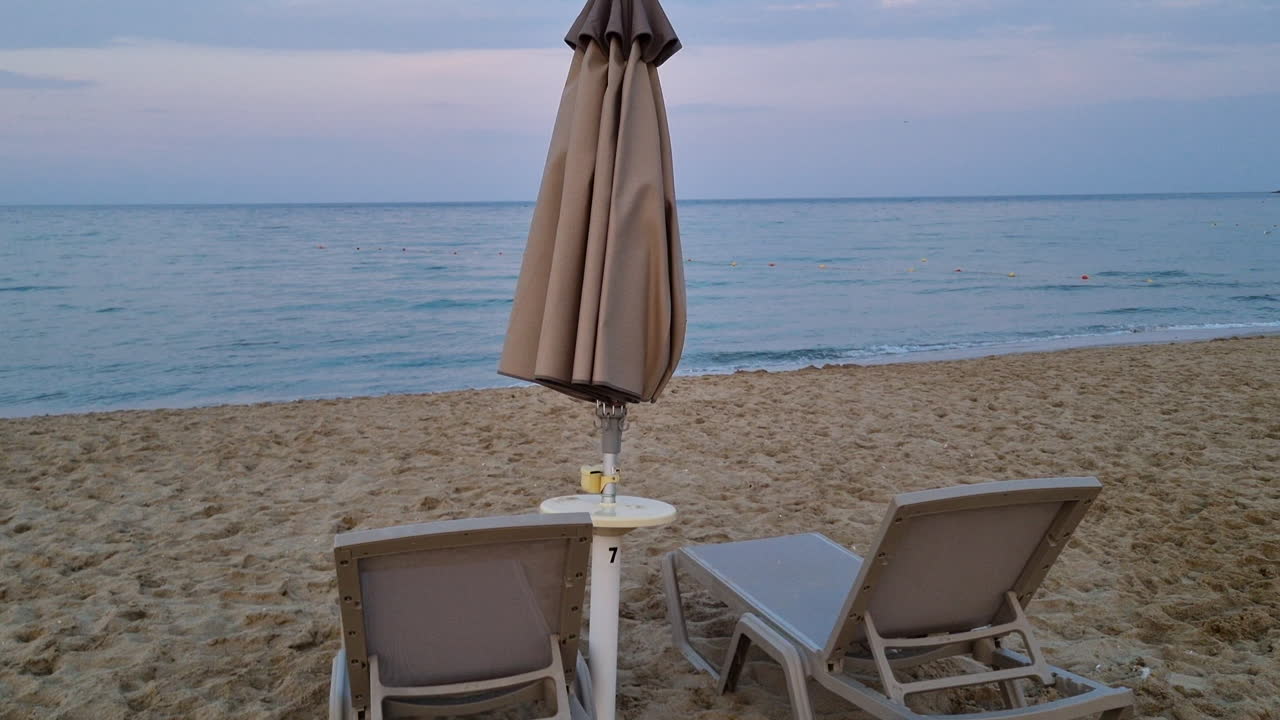 Lettini vuoti e ombrellone chiuso su una spiaggia sabbiosa di sera in una giornata nuvolosa.