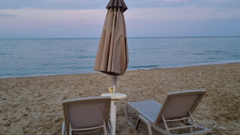 Leere-Sonnenliegen-Und-Geschlossener-Sonnenschirm-An-Einem-Sandstrand-Am-Abend-An-Bewölkten-Tagen