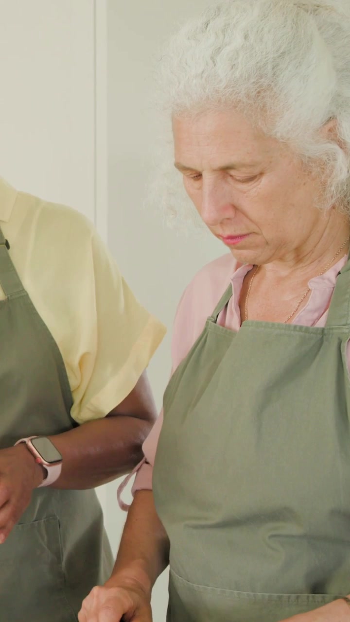 Video verticale: La telecamera si allontana, due donne che affettano peperoni in cucina, grattugiano e preparano con i grembiuli.
