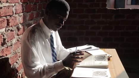 una vista lateral en cámara lenta de un joven africano con uniforme escolar mientras estudia sus libros en una vieja escuela de ladrillos en áfrica