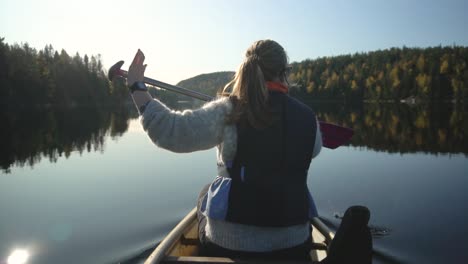 woman paddling canoe boat on beautiful lake in autumn, rear view slow motion