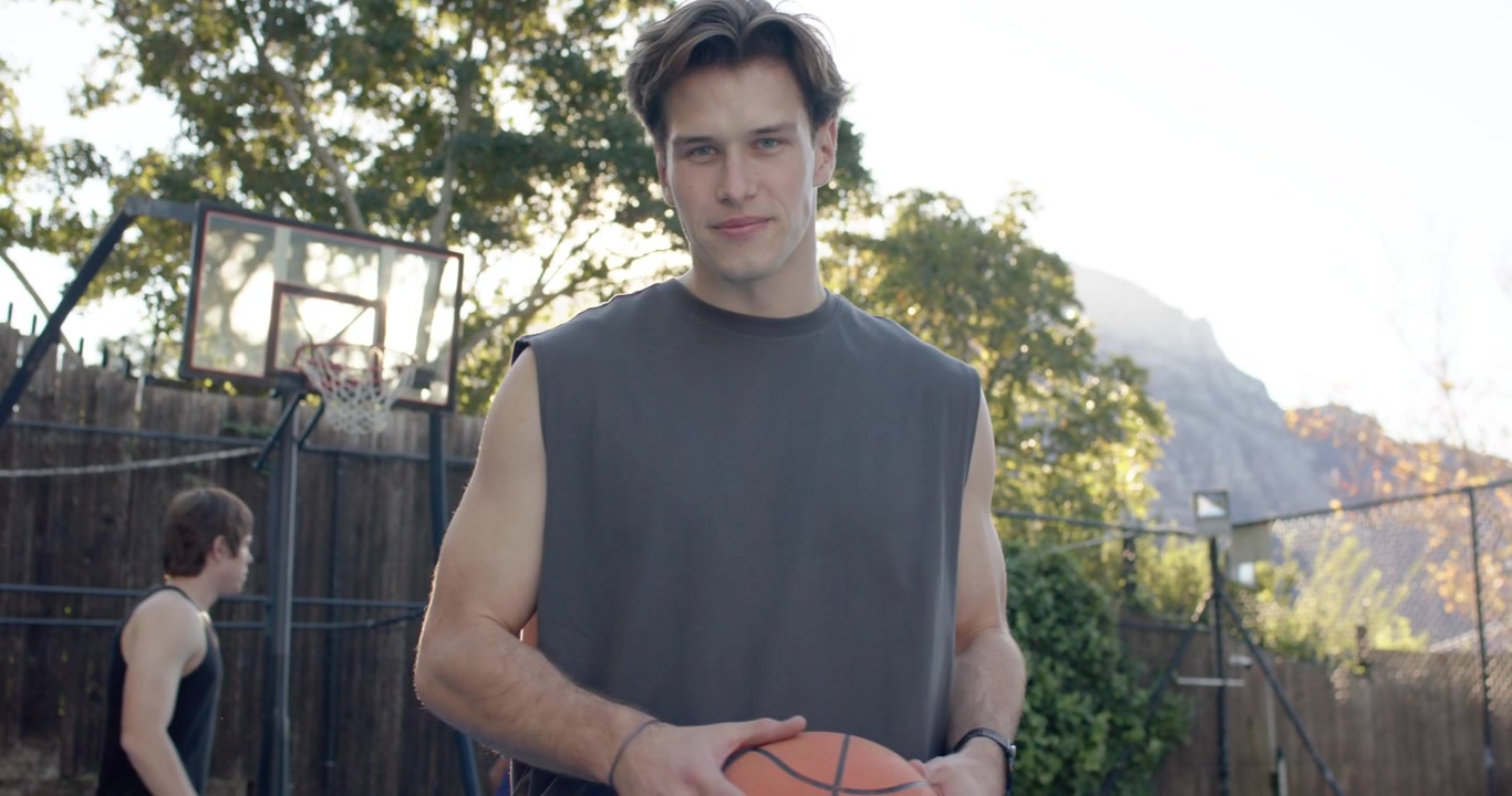 Diverse male friends warming up dribbling basketball on blue court, main player adjusting grip
