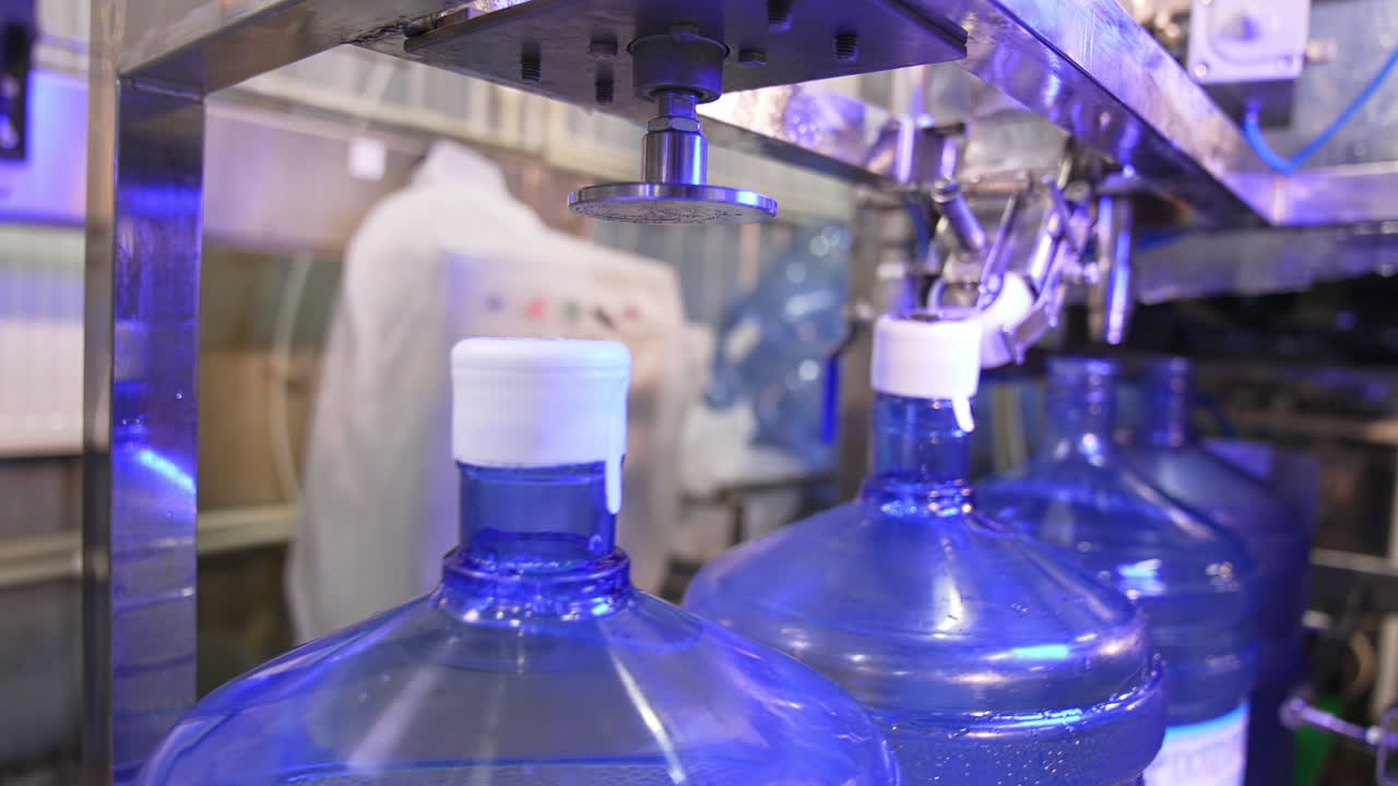 Corking the bottles of fresh clean water. Big flasks filled with water move by the conveyor belt. Mineral water production at factory.